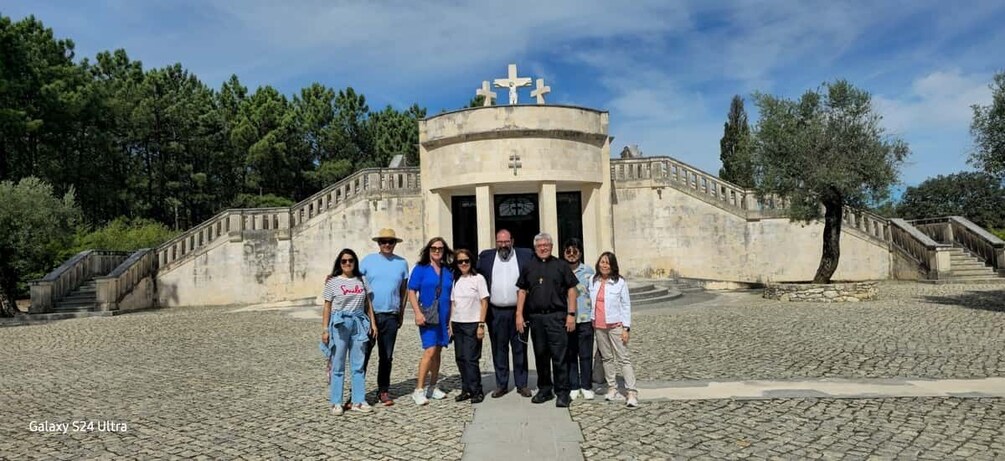 Un grup de persones al davant d'un edifici històric amb una creu a la part superior, envoltat d'arbres i un camí empedrat. 2