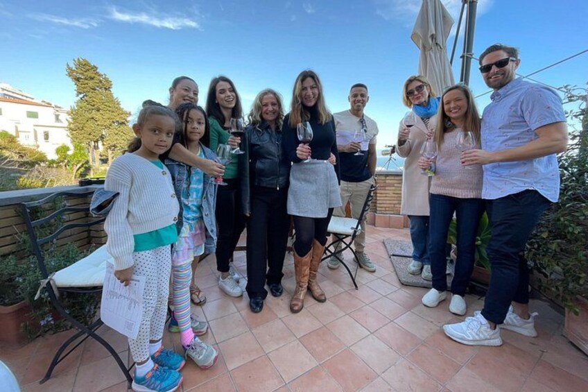A group of people standing on a patio with a tiled floor, outdoor furniture, and a clear sky in the background. 2