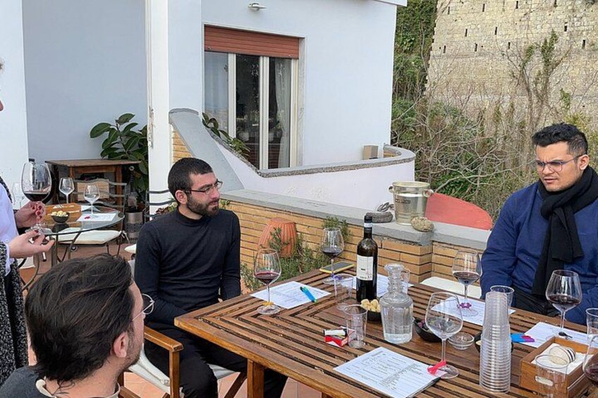 A group of people dining outdoors at a wooden table with wine glasses and bottles. 3