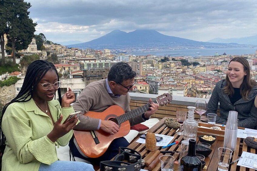 A group of people sitting at a table with a guitar player, a scenic cityscape with a mountain in the background, and a table with glasses and a bottle. 5
