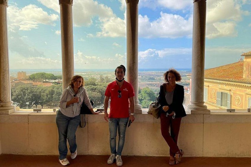 Trois personnes se tiennent dans une colonnade, avec une vue sur la ville en arrière-plan. 1