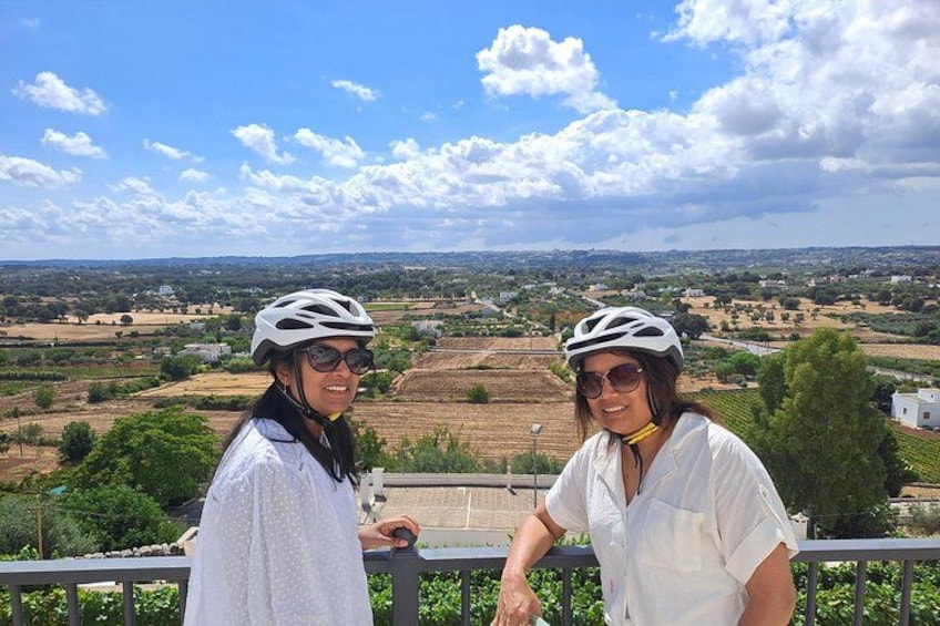 Two people wearing helmets and white shirts standing on a balcony with a view of a rural landscape. 2