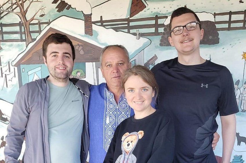 En gruppe mennesker står foran en mural med et hus og et sneklædt landskab. 2