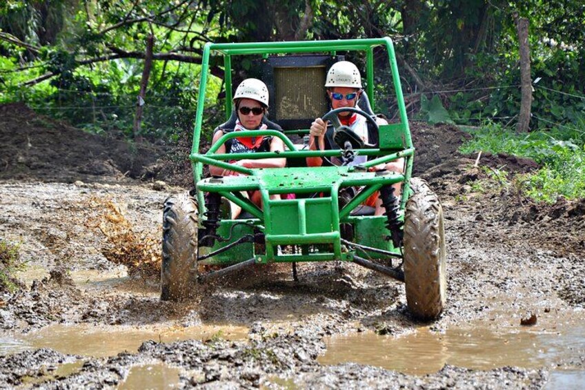 Two people in a green off-road vehicle driving through a muddy terrain. 5