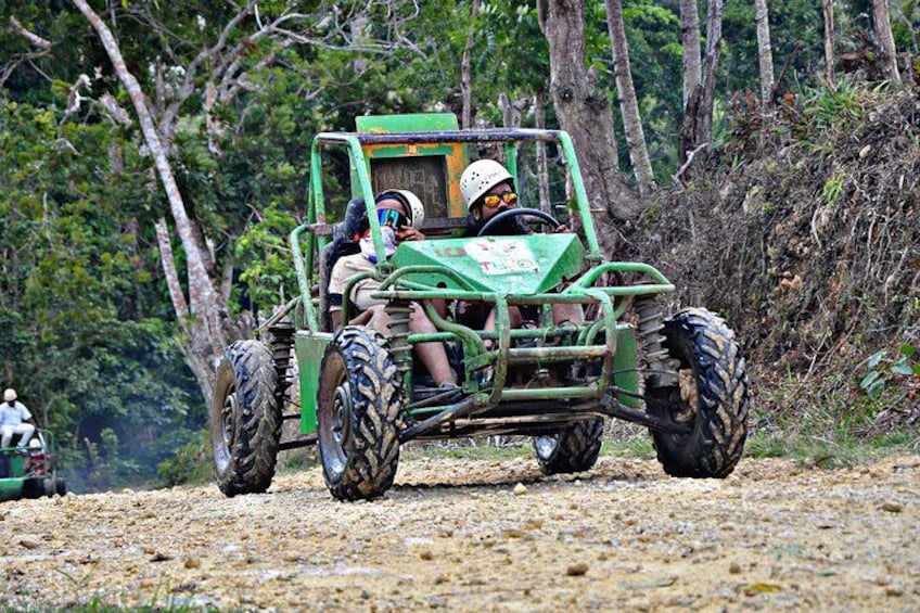 A green off-road vehicle on a dirt path surrounded by trees. 4