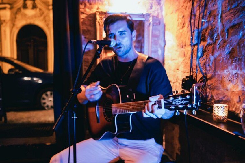 Una persona tocando una guitarra acústica en una habitación con poca luz y un soporte para micrófono. 4