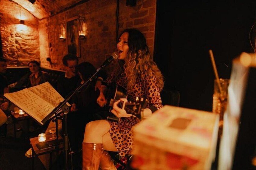 Una persona tocando la guitarra en una habitación tenuemente iluminada, con paredes de ladrillo y una mesa con un menú. 5