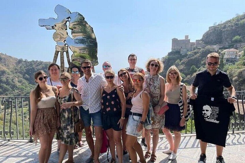 A group of people posing in front of a large sculpture on a bridge with a castle in the background. 4