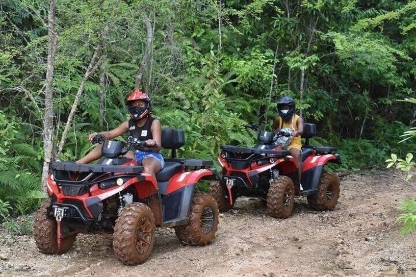 Two people riding ATVs on a dirt path surrounded by dense greenery. 5