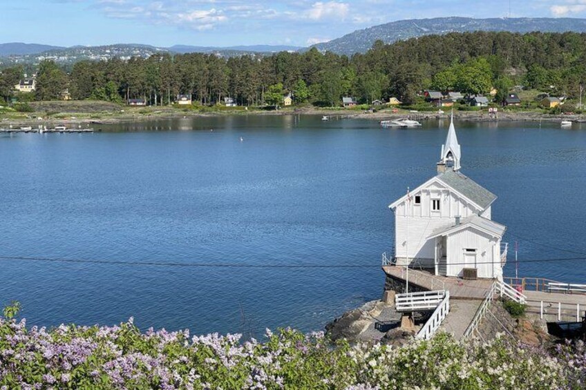 A white church with a steeple on a lakeside, surrounded by trees and houses. 2