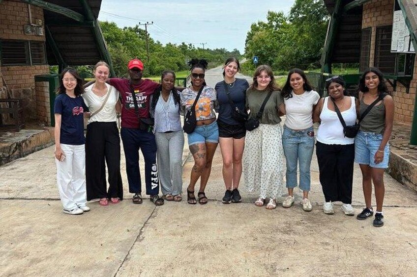 A group of people standing in an outdoor area with a brick building and greenery in the background. 5