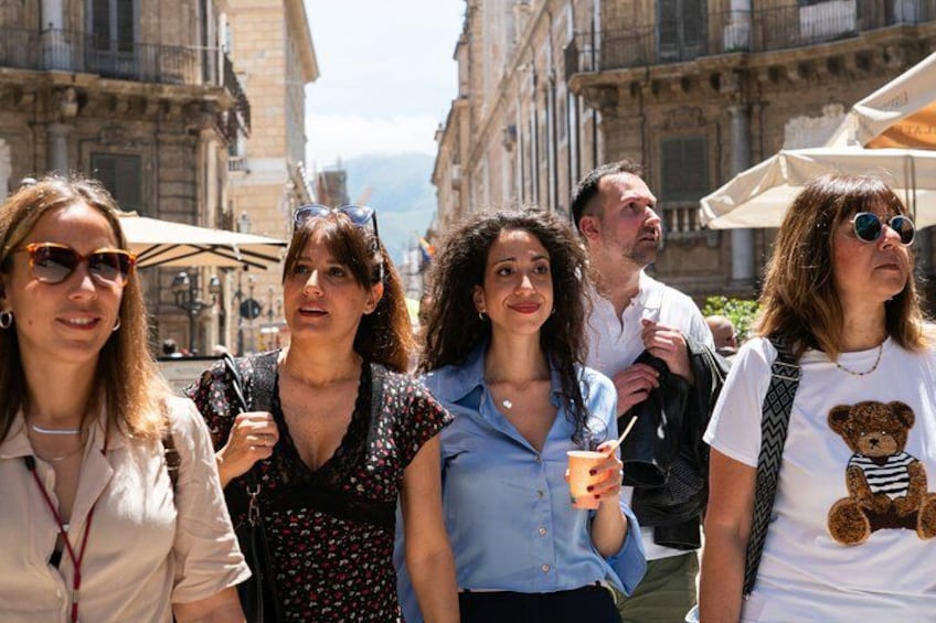 A group of people walking on a street with buildings and umbrellas in the background. 2