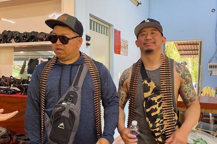 Two men standing in a store with bullet belts and a camera bag. 2