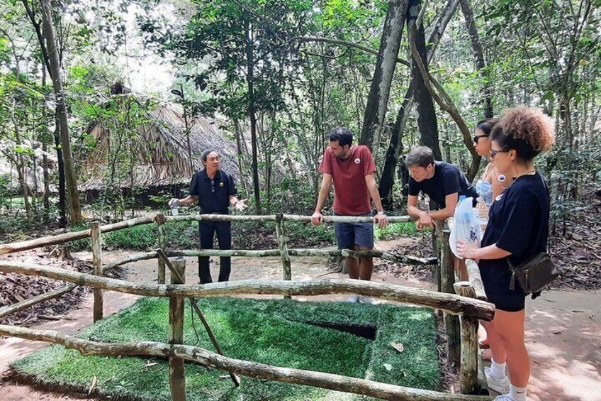Un groupe de personnes observe une zone délimitée par une clôture, recouverte d’un gazon synthétique vert, dans un environnement boisé. 5