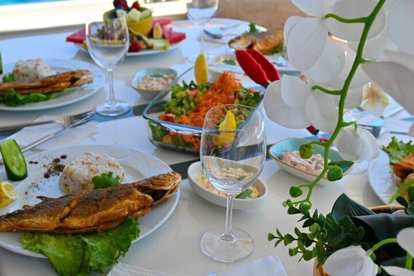 A table with various dishes, including grilled fish, salads, and drinks. 2