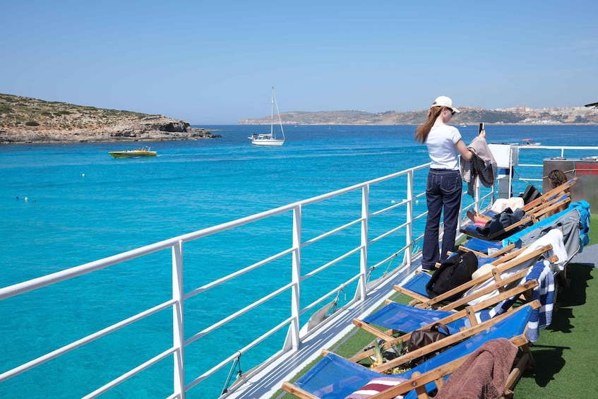 Una donna su una barca, un mare blu e limpido e una costa lontana con edifici. 4