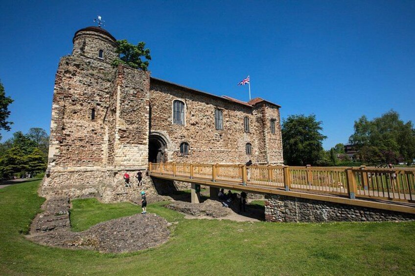 A historic stone building with a tower, a wooden bridge, and a flag. 1