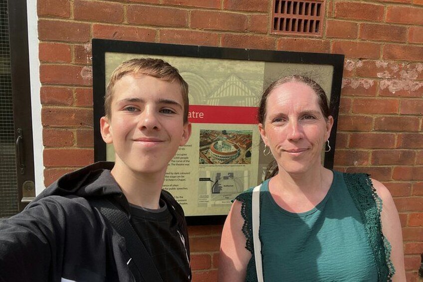 Two people standing in front of a brick wall with a framed poster. 3