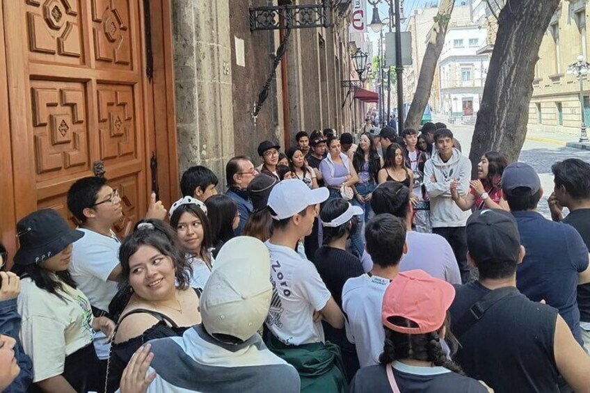 Un grupo de personas reunidas frente a un edificio con una puerta de madera grande. 4