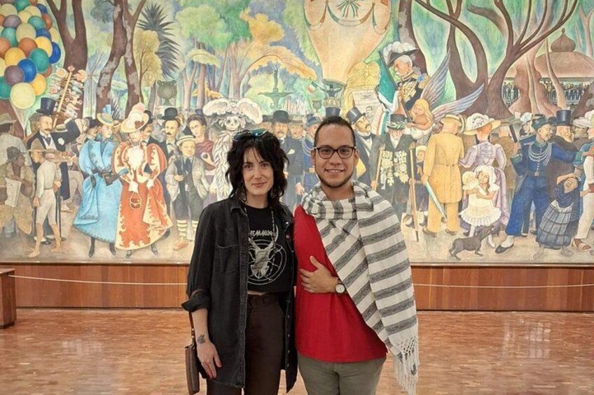 Due persone davanti a un murale raffigurante personaggi storici e un paesaggio tropicale. 5