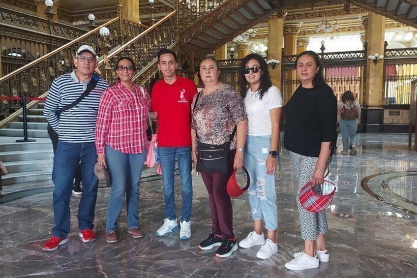 Un grupo de personas de pie en un edificio imponente y ricamente decorado, con piso de mármol y una escalera. 2