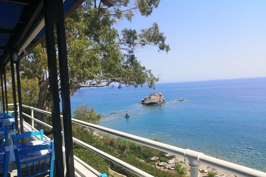 A coastal view with a rocky outcrop, clear blue sea, and a balcony with blue chairs. 5