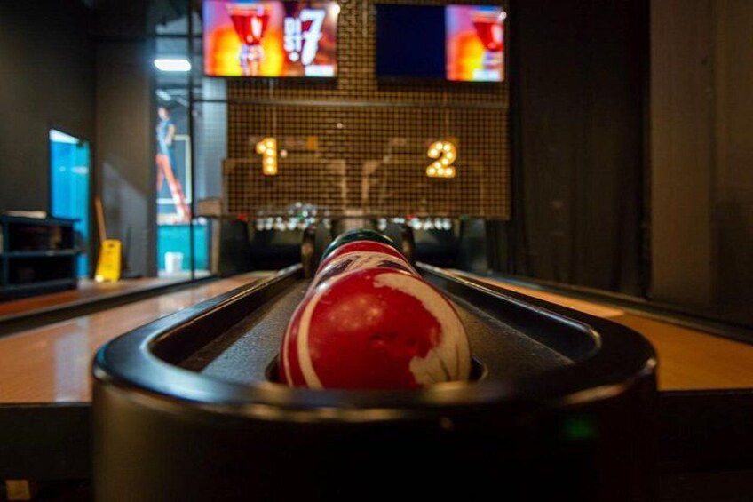 Eine Kegelbahn mit einem Bowlingball im Vordergrund und einer Anzeigetafel im Hintergrund. 2