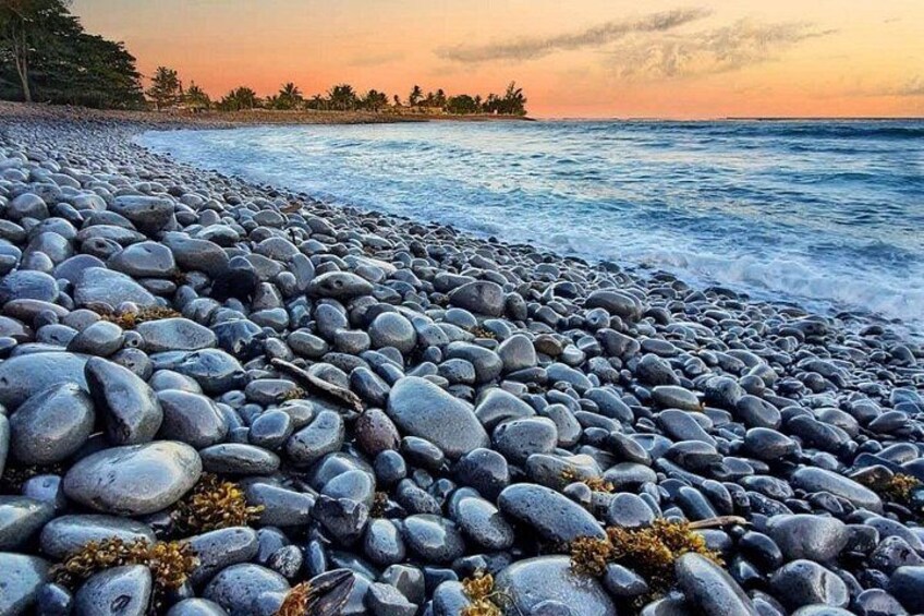 Una playa de guijarros con olas, árboles y una puesta de sol. 3