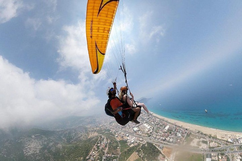 Une personne pratiquant le parapente au-dessus d’une zone côtière, avec une vue dégagée sur la plage et la ville en contrebas. 4