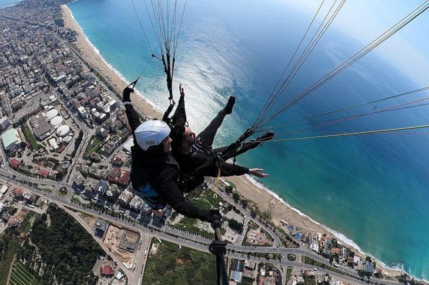 Une personne pratiquant le parapente au-dessus d’une zone côtière, avec une plage et un paysage urbain en contrebas. 2