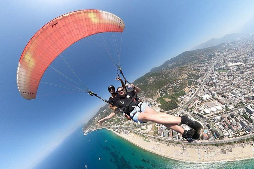 Une personne pratiquant le parapente au-dessus d’une ville côtière, avec une vue dégagée sur la plage et le paysage urbain en contrebas. 3