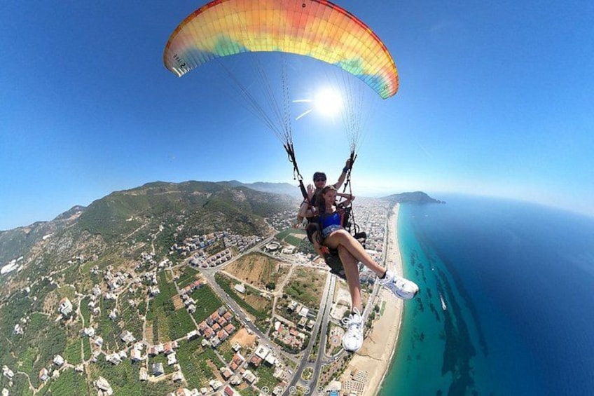 Une personne pratiquant le parapente au-dessus d’une zone côtière, avec une plage et une ville en contrebas. 1