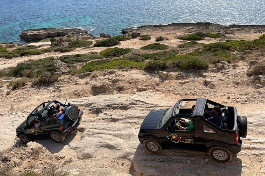 Twee offroad voertuigen op een rotsachtig strand, met de zee op de achtergrond. 2