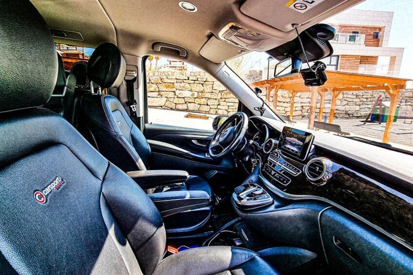 A car interior with black leather seats, a steering wheel, a dashboard with a screen, and a gear shift. 3