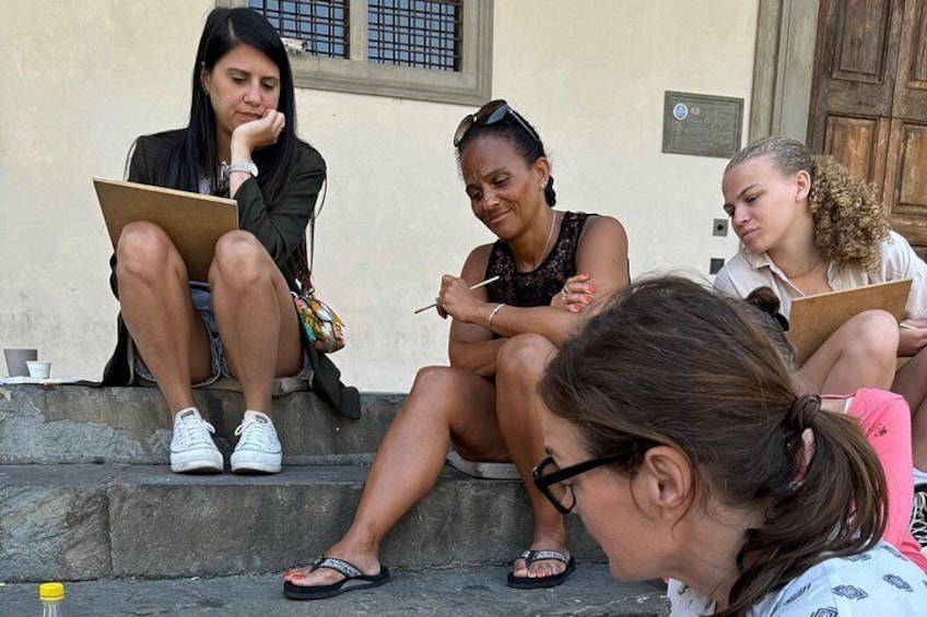 Three people sitting on steps, one holding a clipboard, another holding a pen, and the third looking at a notebook. 4