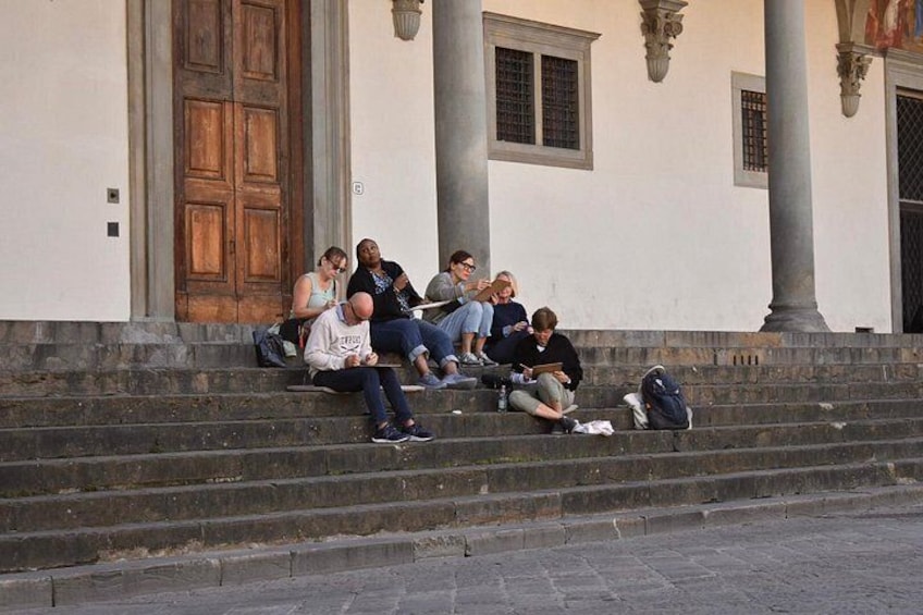 A group of people sitting on steps in front of a building with columns and a wooden door. 2