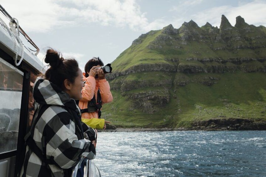 Un bote con gente fotografiando una costa montañosa. 4