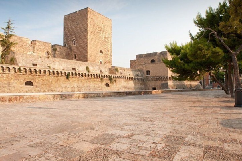 A historic stone fortress with a prominent tower, a paved courtyard, and a tree. 5