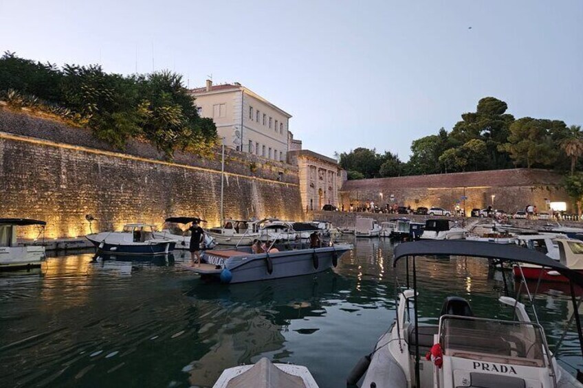 Ein Yachthafen mit vertäuten Booten, eine Steinmauer und Gebäude im Hintergrund. 4