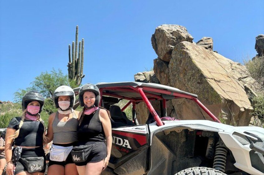 Two people in riding gear, a red off-road vehicle, and a desert landscape with cacti. 3