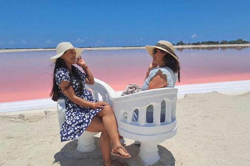 Two people sitting on a white bench by a pinkish water body. 1