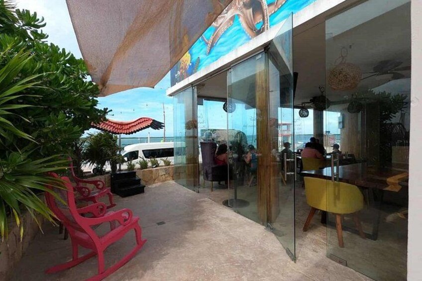 An outdoor seating area with glass walls, red chairs, and a tropical plant. 5