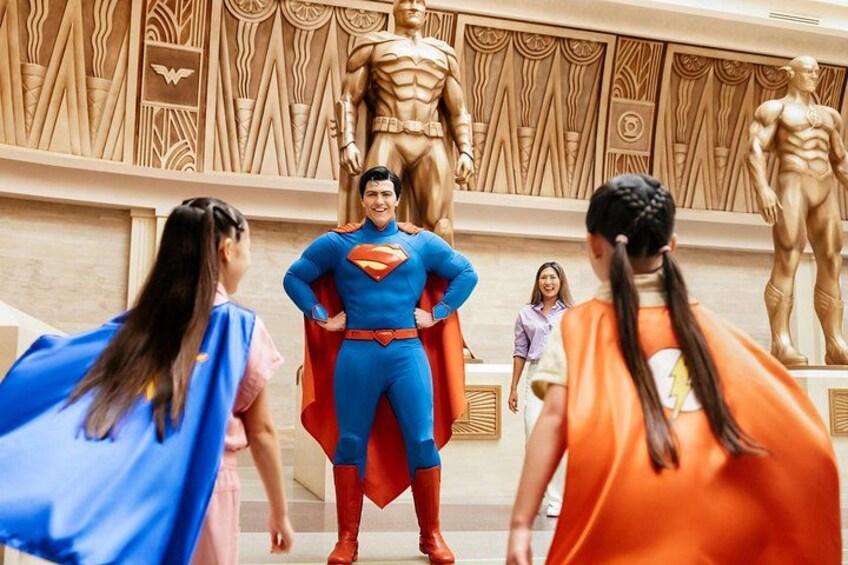 A person in a Superman costume standing in front of a large wooden sculpture. 1