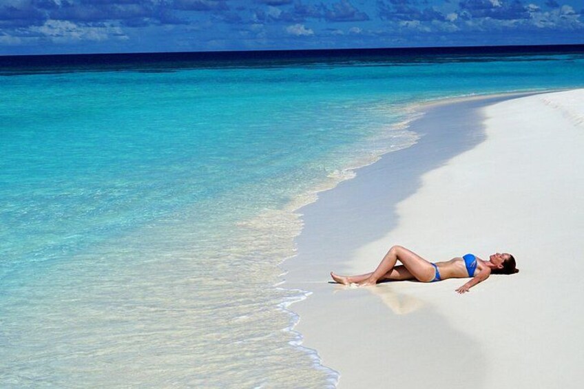 Iemand ligt op een wit zandstrand met helder turquoise water. 5