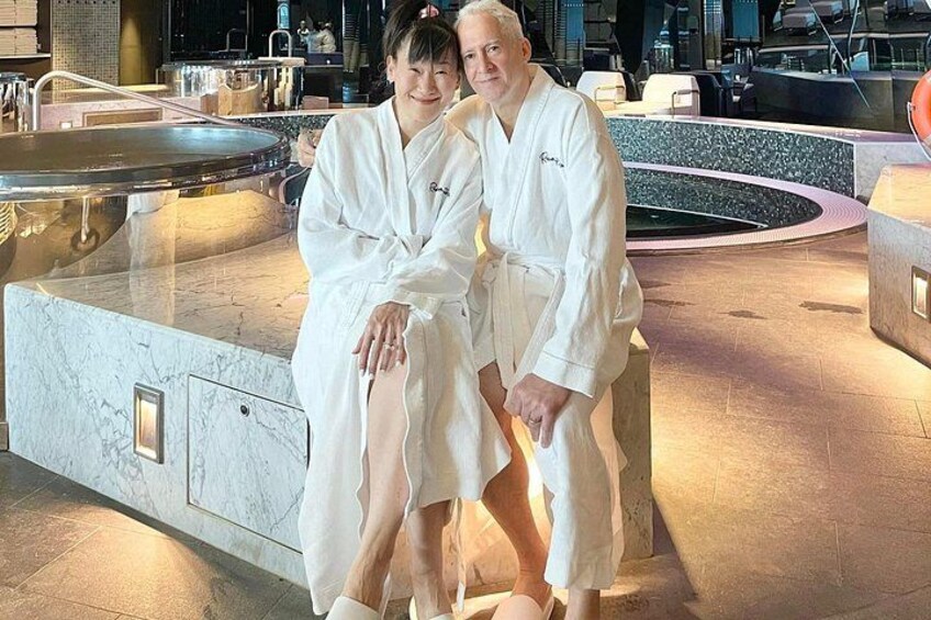 Deux personnes vêtues de longues robes blanches sont assises au bord d’une piscine de spa dont le sol est en marbre et dont le design est moderne. 3
