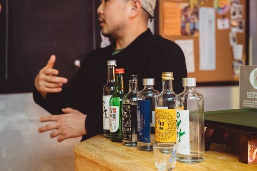 A person gesturing near a table with various bottles of alcohol. 1