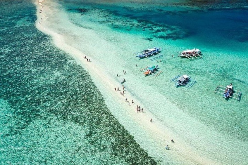 A beach with clear turquoise water, people walking, and traditional boats anchored. 1