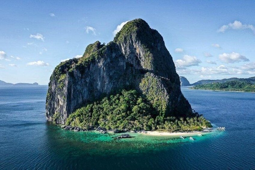 A large limestone island surrounded by clear blue waters, with lush greenery and a small beach. 3