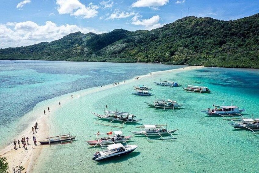 A beach with boats, people, and a forested hill. 2