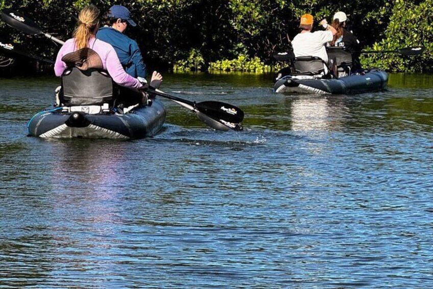 People in inflatable boats on a calm body of water surrounded by greenery. 4